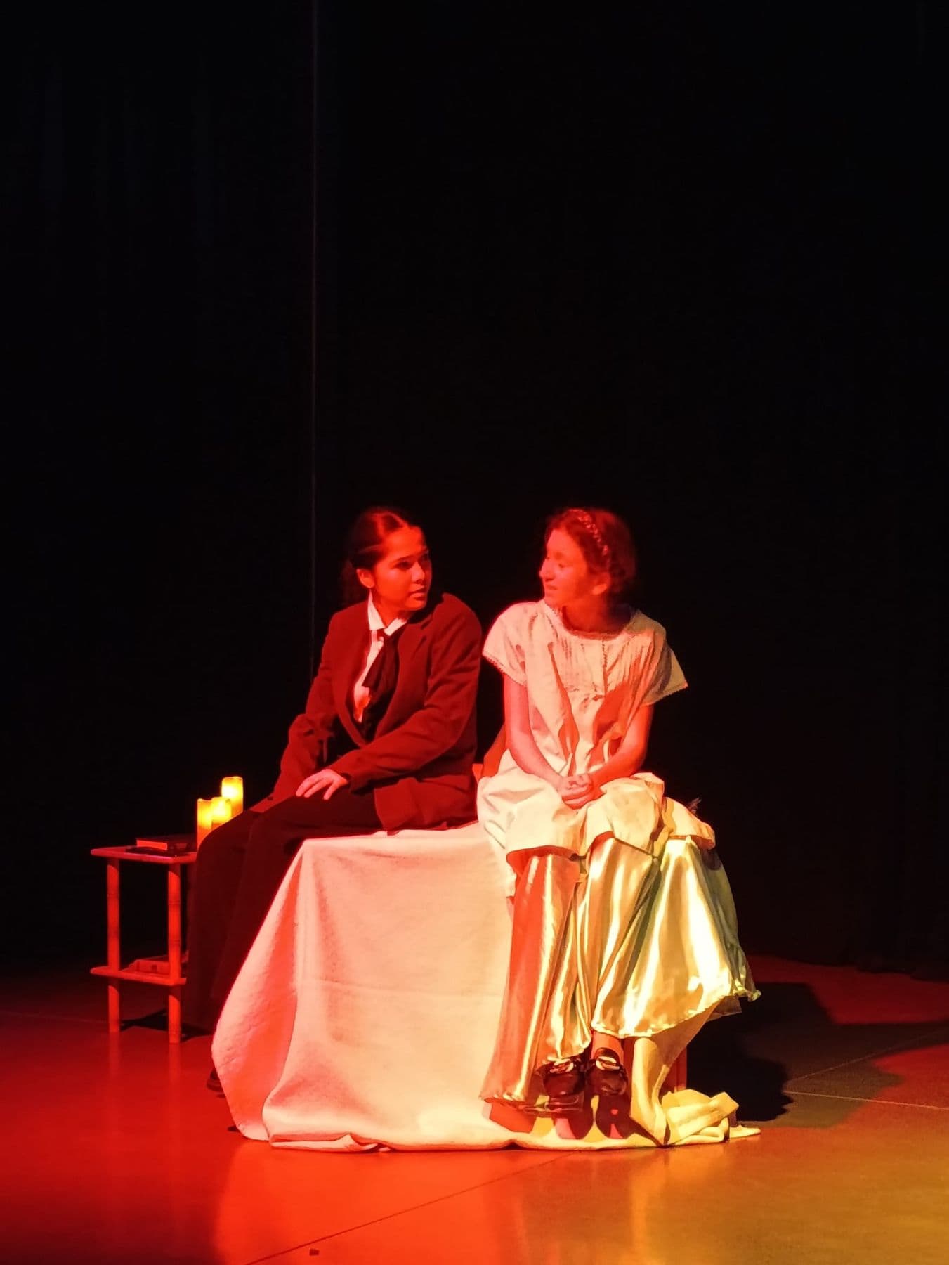 Two young actors on stage, bathed in red light.