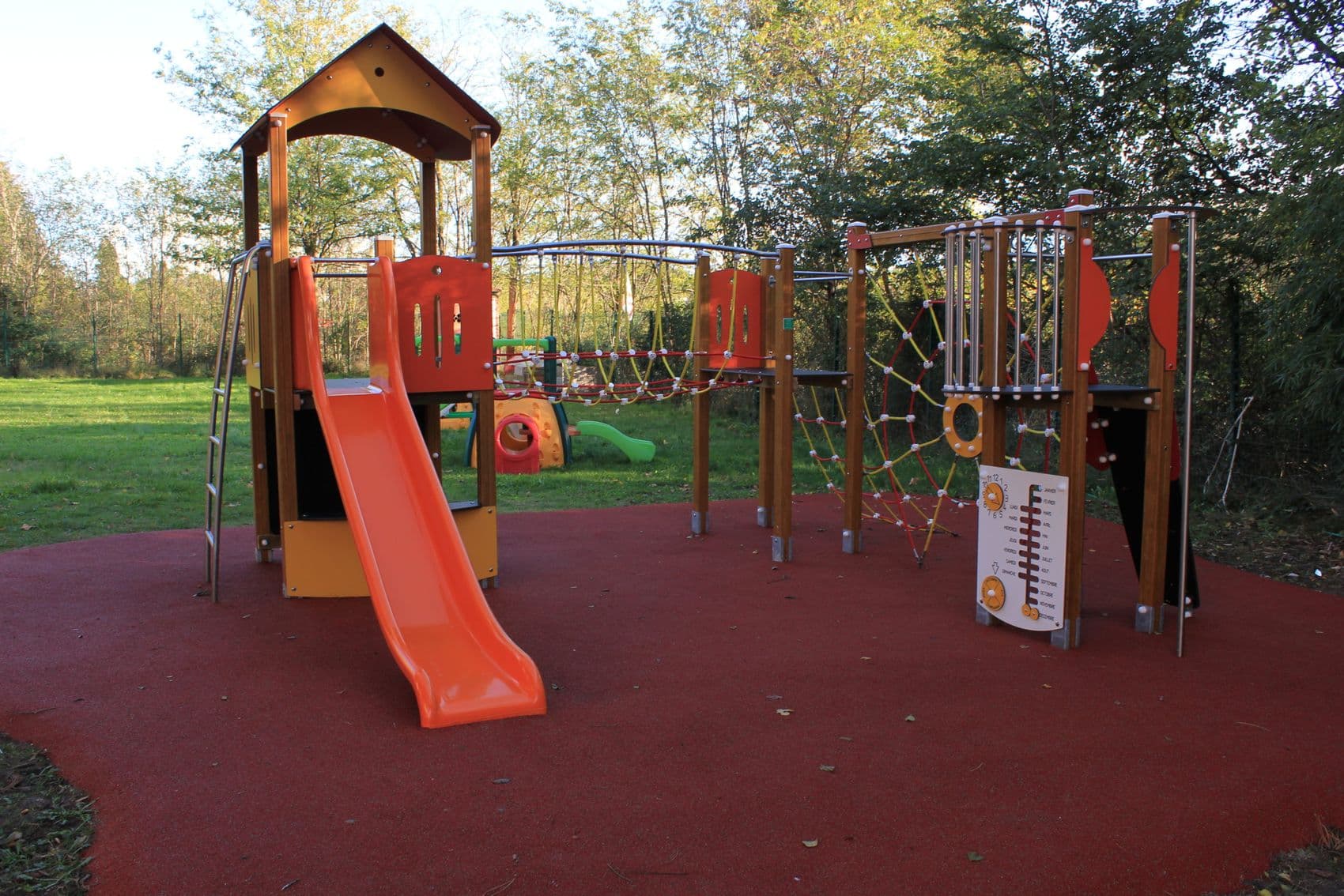 L'aire de jeux, avec son toboggan et son filet d'escalade, entourée d'arbres.