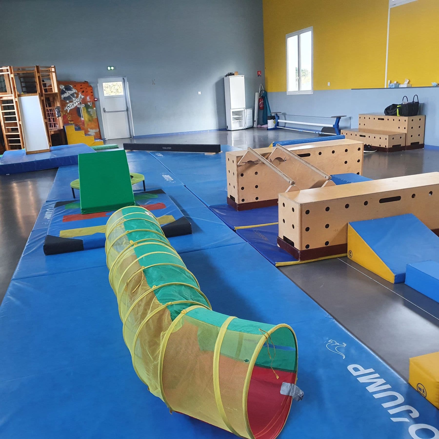 Le gymnase aménagé en parcours de motricité, avec tapis, poutres et tunnel.