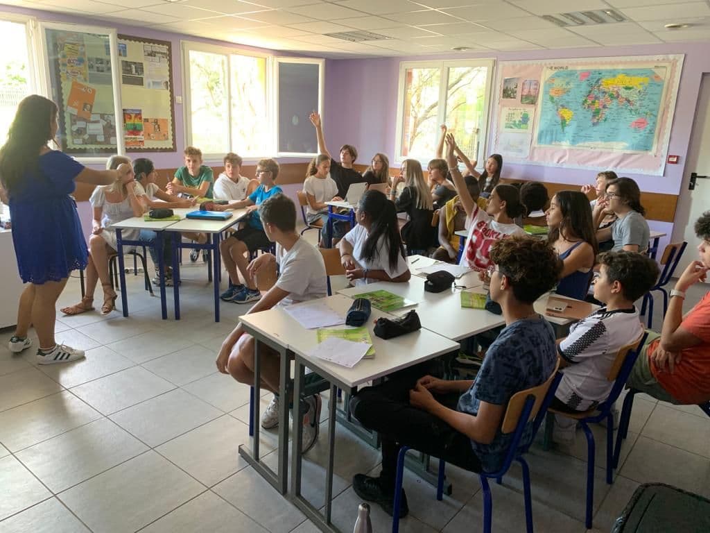In class, middle school pupils raise their hands to ask questions.