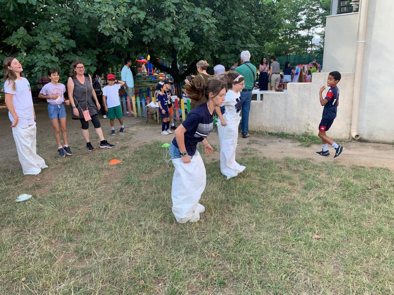 A sack race on the grass, under the trees, during the school fair.