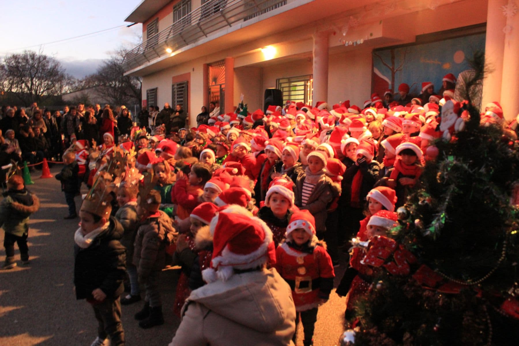 Spectacle de Noël à la tombée de la nuit : les élèves en bonnet rouge devant l'école.