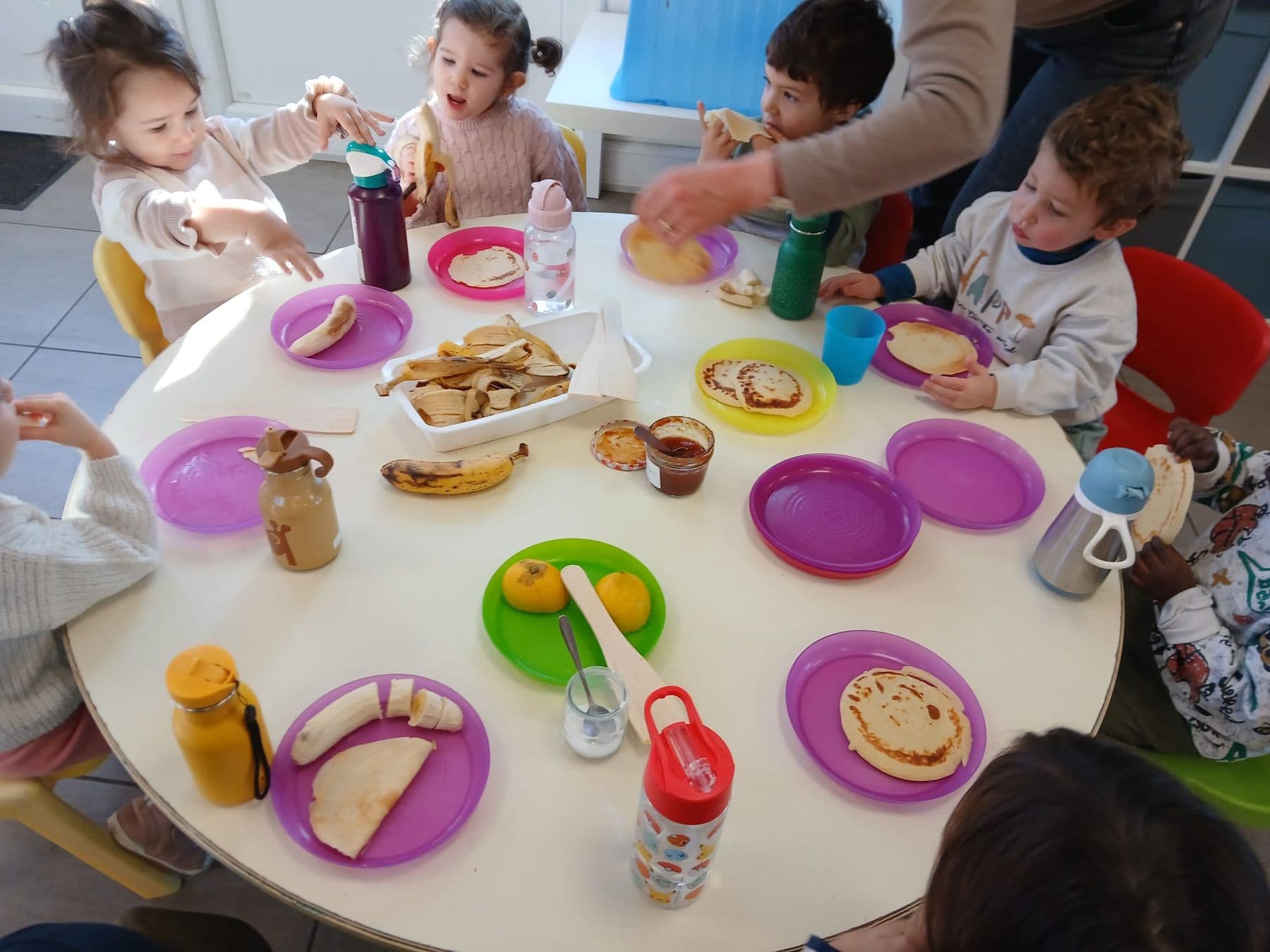 L'heure du goûter en maternelle : crêpes et bananes dans des assiettes colorées.